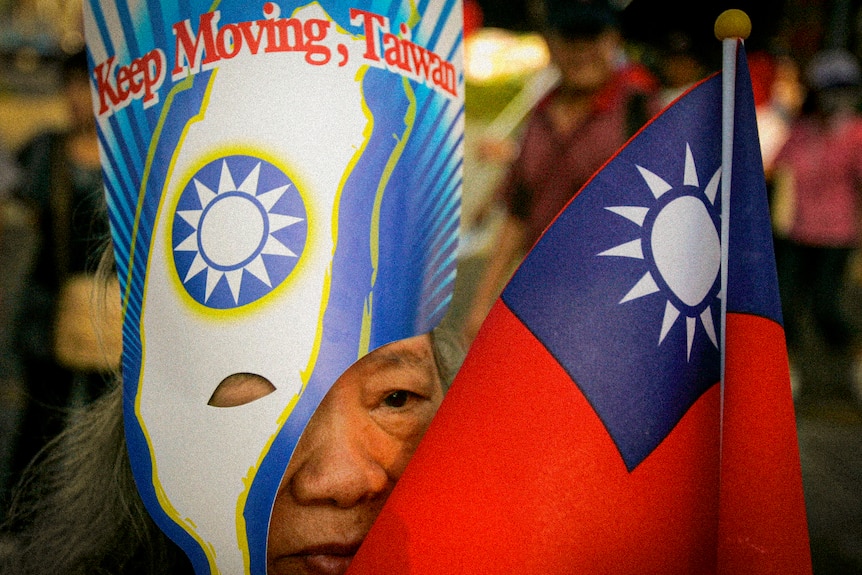 An older Taiwanese woman in a mask with 'Keep Going Taiwan' while her face is obscured by a Taiwanese mask