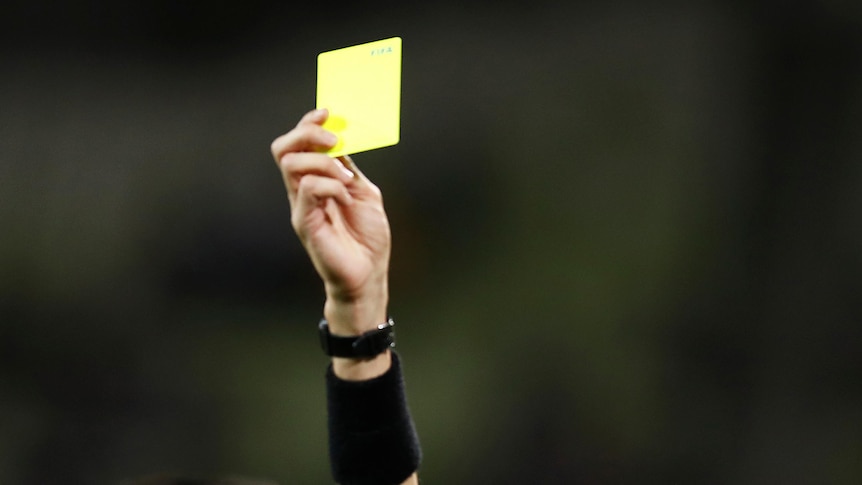 A yellow card is held up by a referee