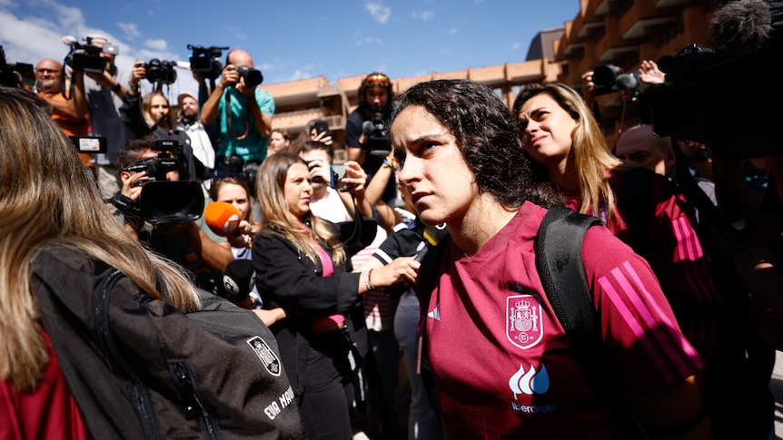 A group of women arrive at a hotel, surrounded by media.