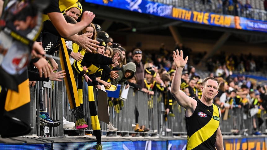 A Richmond AFL star holds his hand up to salute a group of Tigers fans who are standing at the fence after a win.