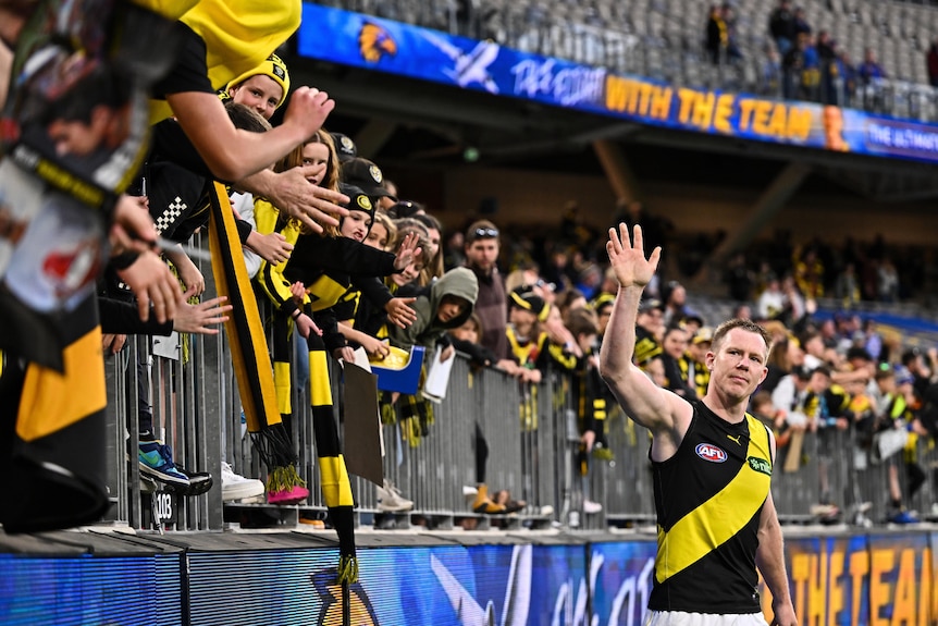 A Richmond AFL star holds his hand up to salute a group of Tigers fans who are standing at the fence after a win.