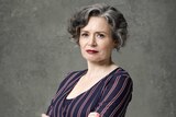 The comedian Judith Lucy, grey hair and bright red lipstick stares determinedly with arms crossed