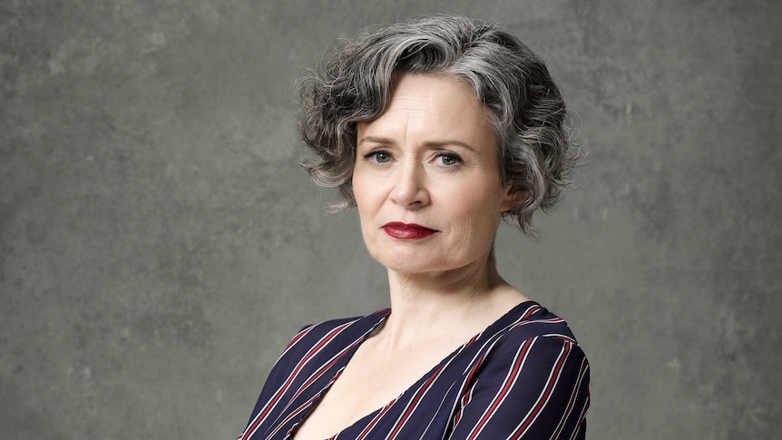 The comedian Judith Lucy, grey hair and bright red lipstick stares determinedly with arms crossed