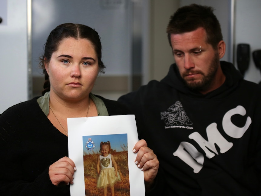 A woman holding a picture of a small girl, next to a man.