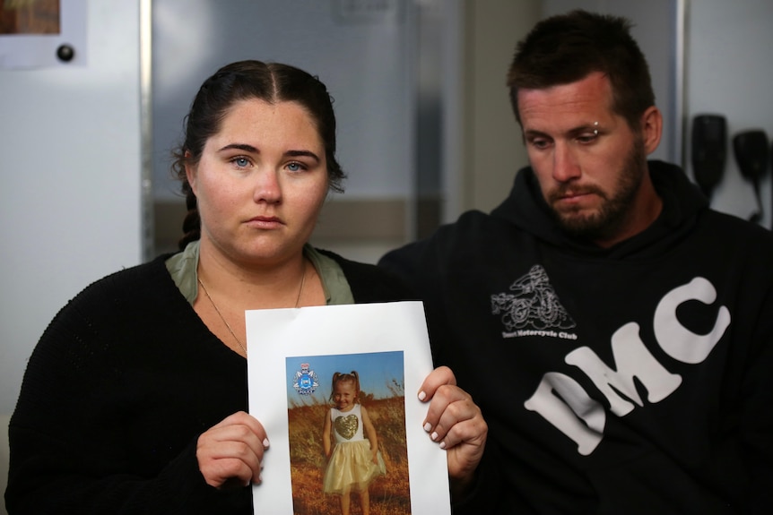 A woman holding a picture of a small girl, next to a man.