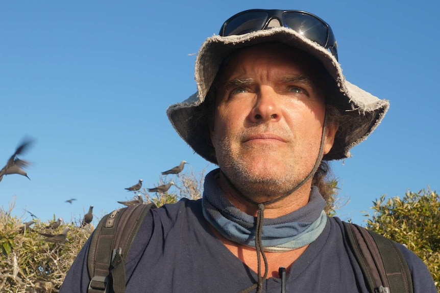 A close-up picture of a man in a hat with seabirds flying in the background