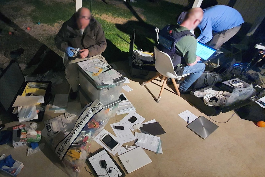 Officers are pictured with evidence bags nd computers in the backyard of a home.