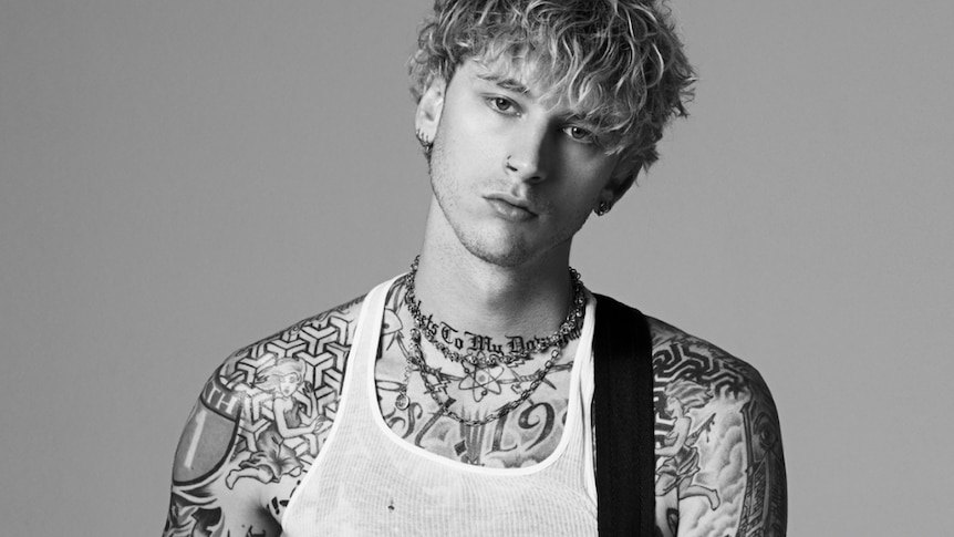 Black and white image of Machine Gun Kelly; subject in white singlet, holding guitar