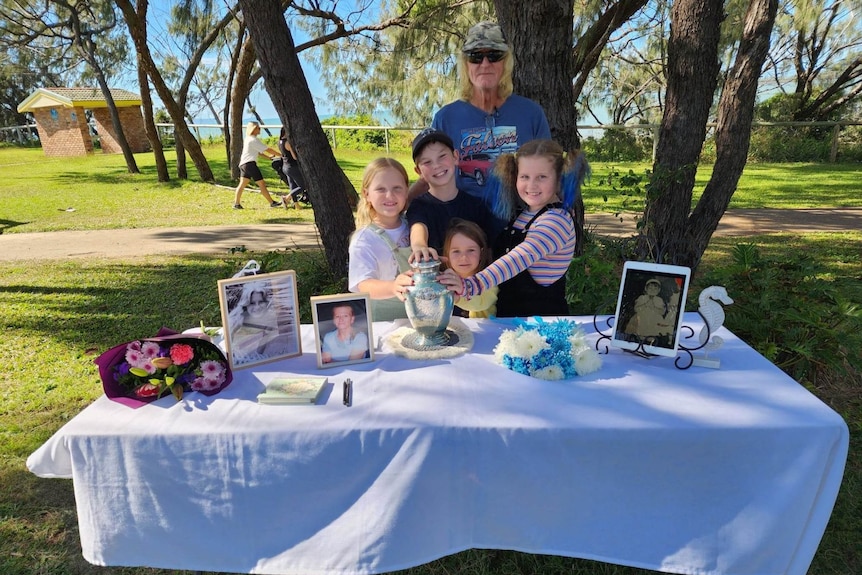 A man stands with small children in front of a table with flowers and photos