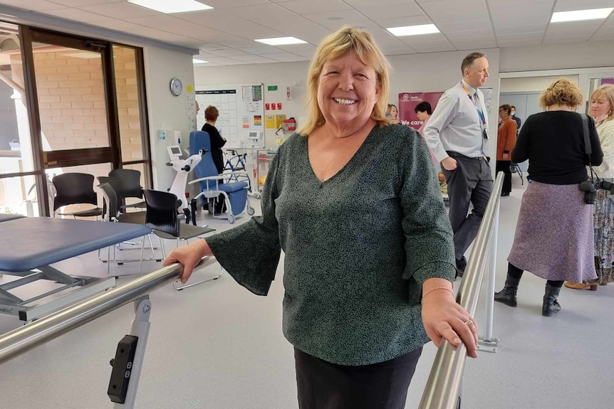 an older woman with blonde hair holding onto walking assist bars in a hospital ward
