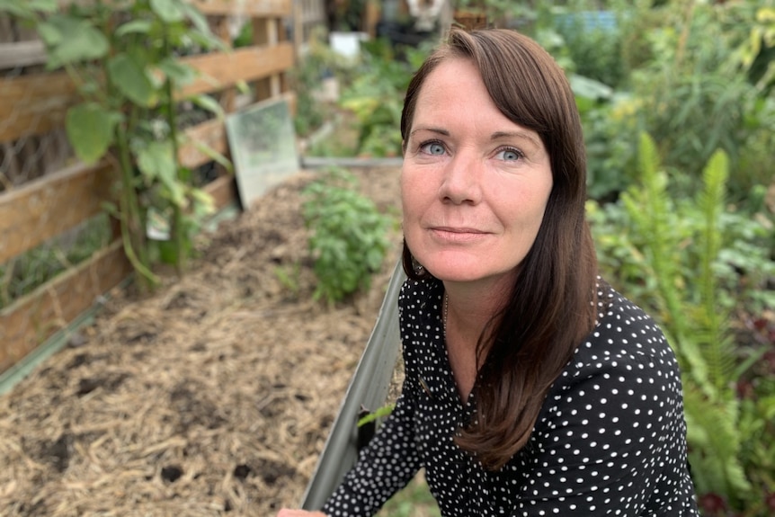 A woman kneels beside a garden bed.