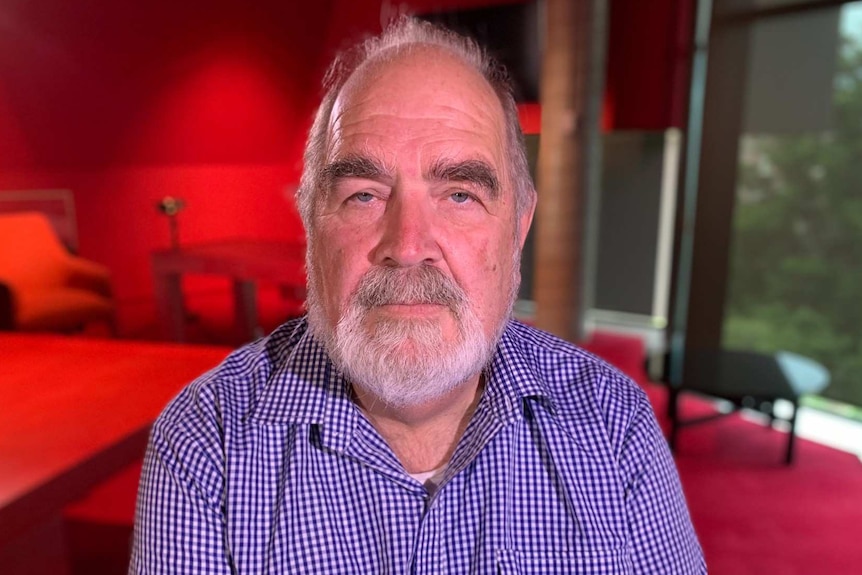 David Bowen looks into the camera as he poses for a photo in a room bathed in red light.