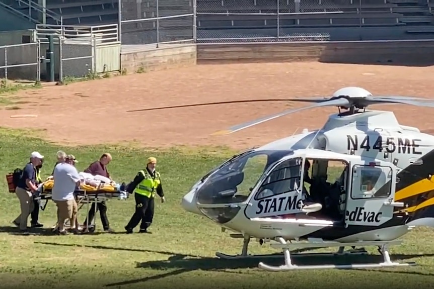 A stretcher bed is wheeled to helicopter waiting on a grass field