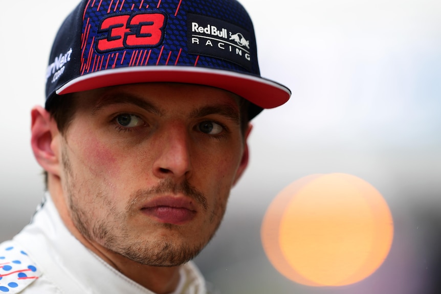 Race driver wearing a blue cap stares off into the distance. 