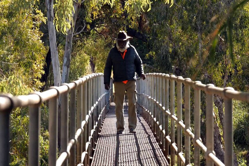 An Indigenous man crosses a narrow pedestrian bridge.