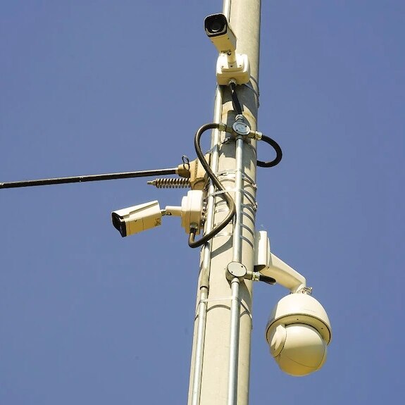 A street pole of surveillance cameras on a blue day.