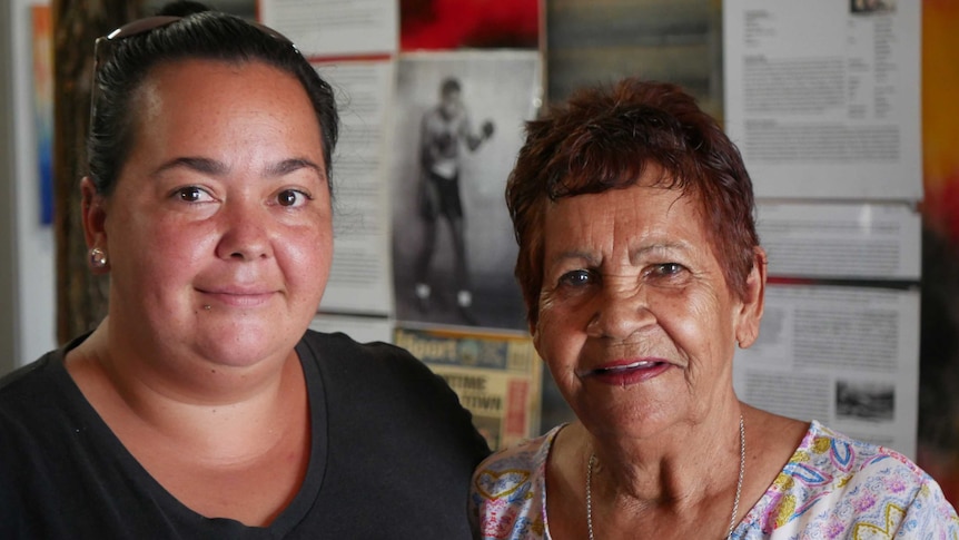 Aboriginal woman and Aboriginal elder woman smile in art gallery.