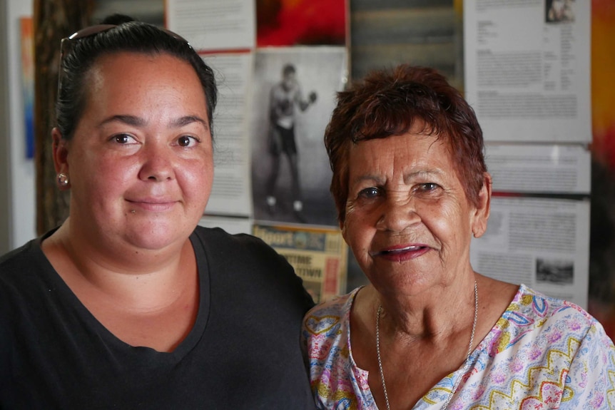 Aboriginal woman and Aboriginal elder woman smile in art gallery.