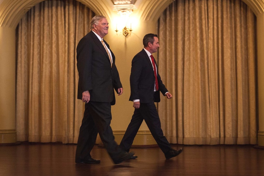 A profile shot of former federal opposition leader Kim Beazley walking with Premier Mark McGowan in a ball room.