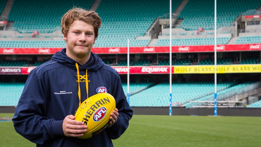 AFL player Dylan Donaldson holding a football, standing on Sydney Cricket Ground with AFL goal posts in the background.