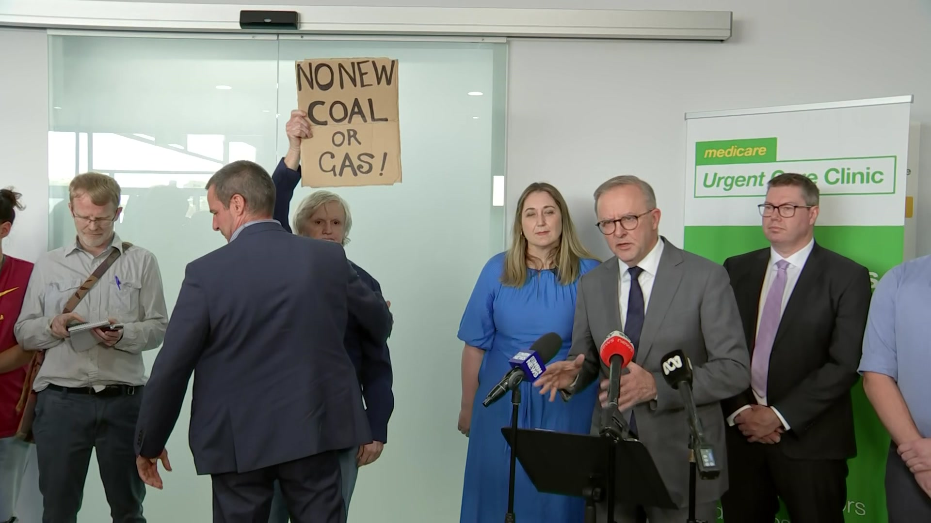 Anthony Albanese addresses the media. A climate change activist can be seen nearby.