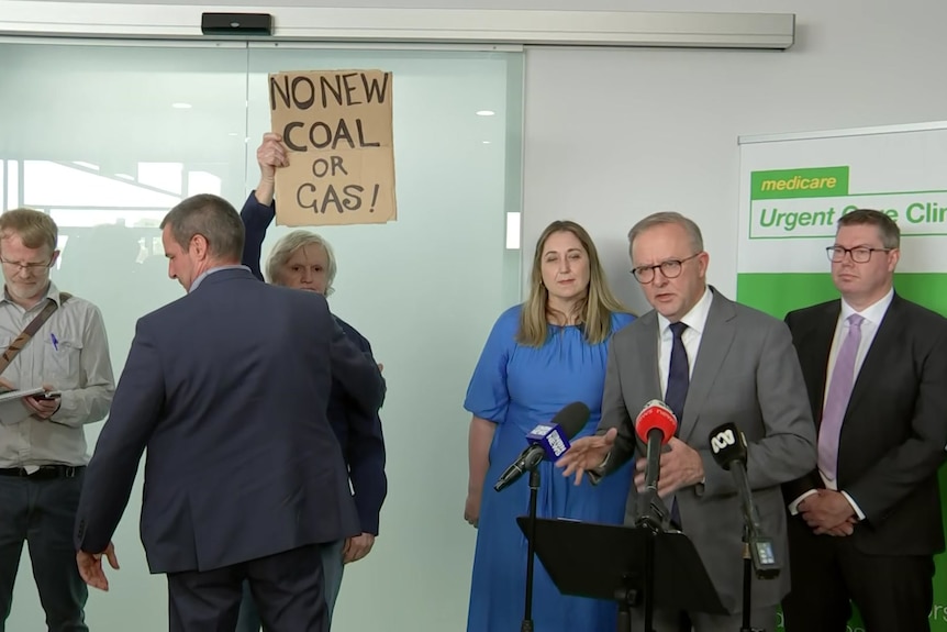 Anthony Albanese addresses the media. A climate change activist can be seen nearby.