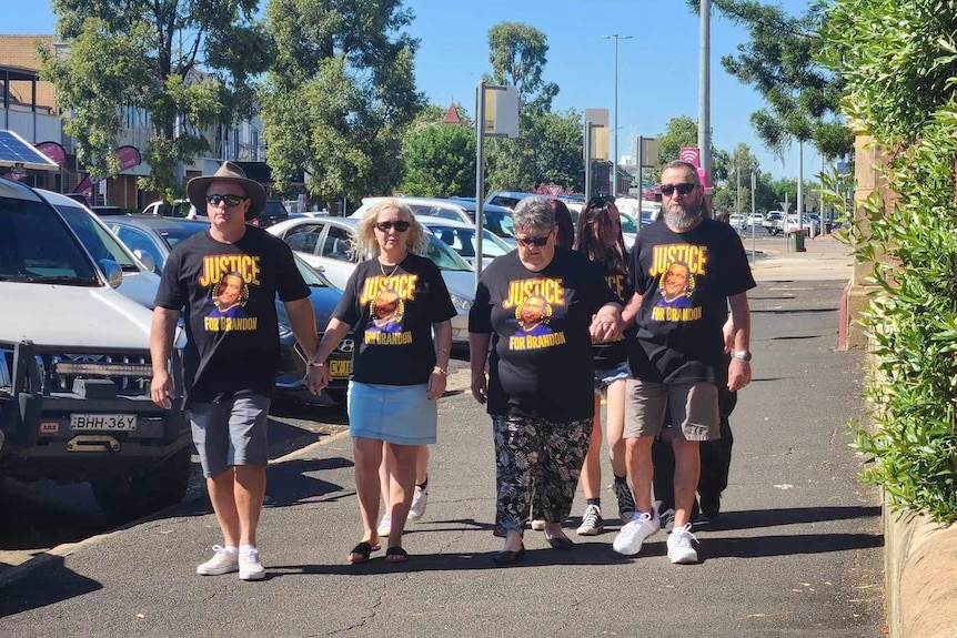 A group of people walk toward the camera wearing 'justice for brandon rich' shirts.