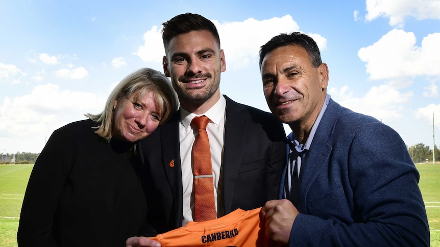A man with his mum and dad holding a sports t-shirt.