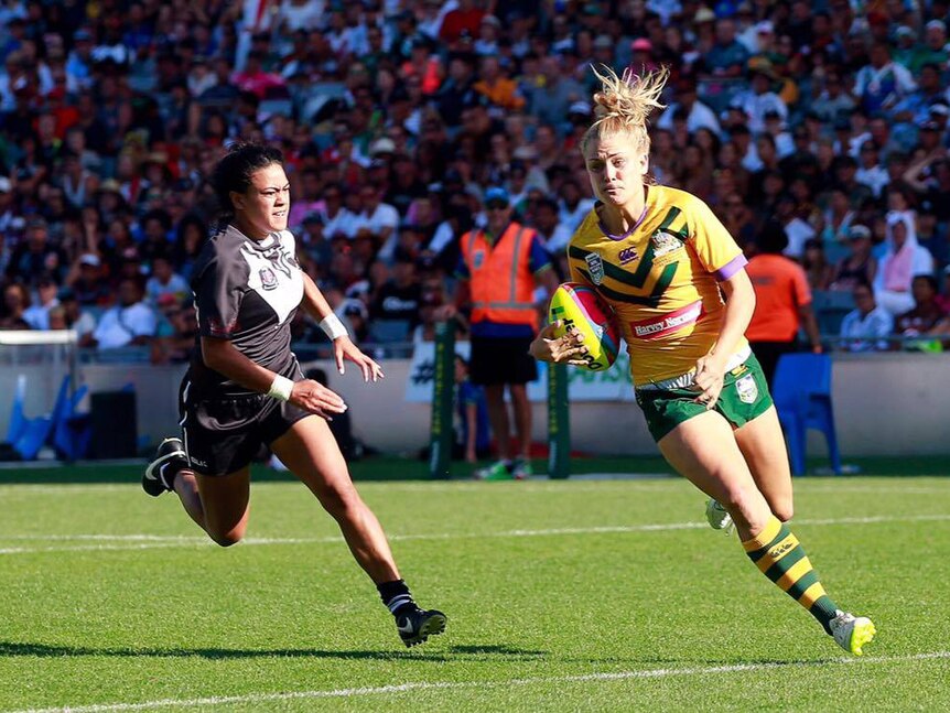 A New Zealand player chases Kody House who has the ball, crowd blurry in background