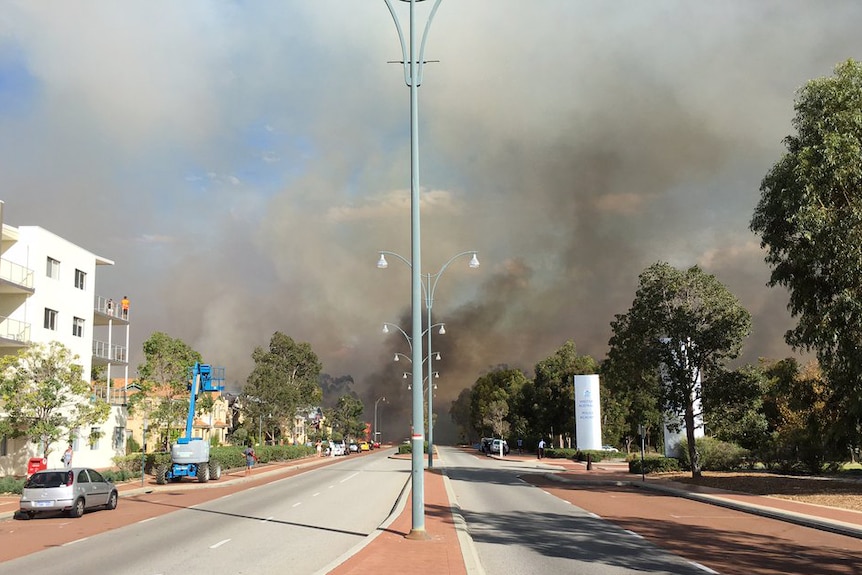 Thick black smoke rises into the sky from a bushfire at the end of a road in Joondalup.