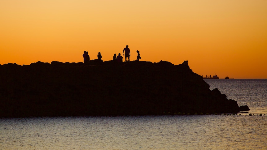 People standing on the rocks at sunset at a groyne