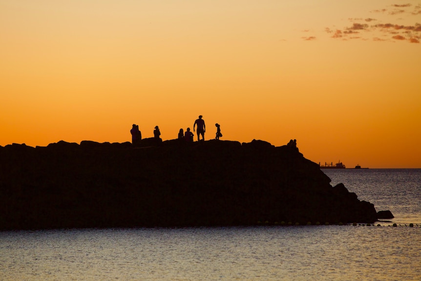 People standing on the rocks at sunset at a groyne