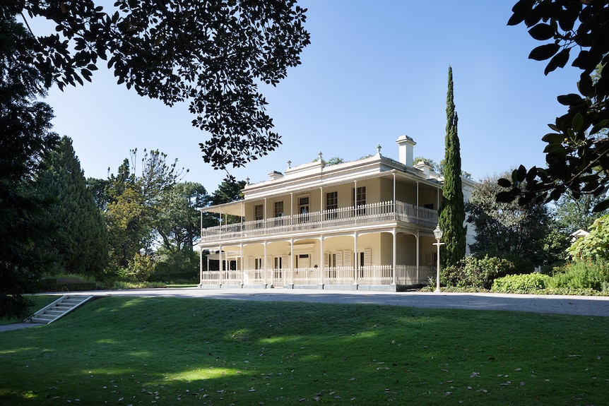 Grand white house with balconies on a sweeping green lawn 