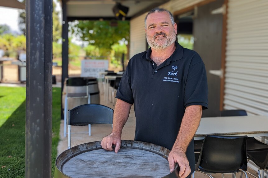 Bruce Heward, a middle-aged man with a beard and grey hair, stands in front of a wine barrel outside a corrugated iron bar 
