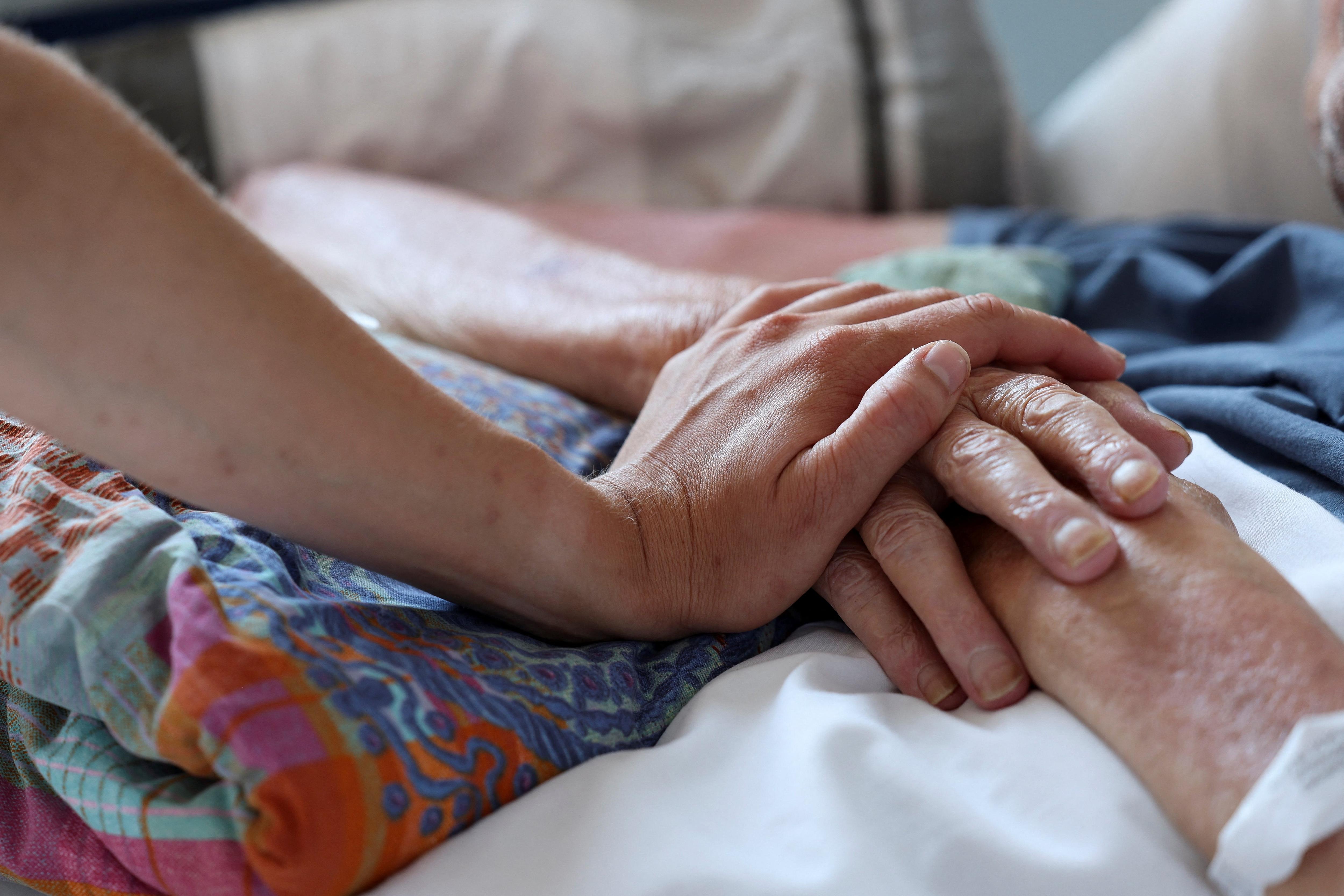 A nurse touches the hand of a patient in palliative care
