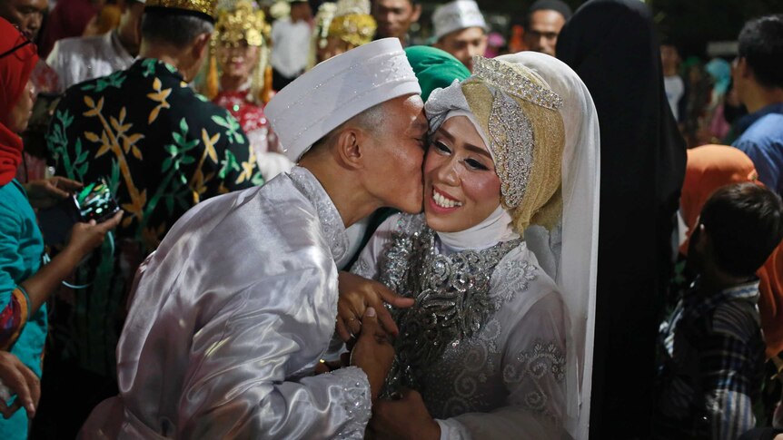 A bride and groom wearing traditional dress embrace.