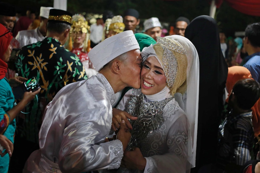 A bride and groom wearing traditional dress embrace.