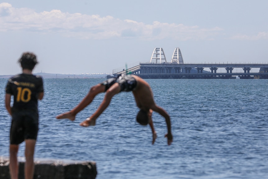 Kids jump into the sea near a bridge