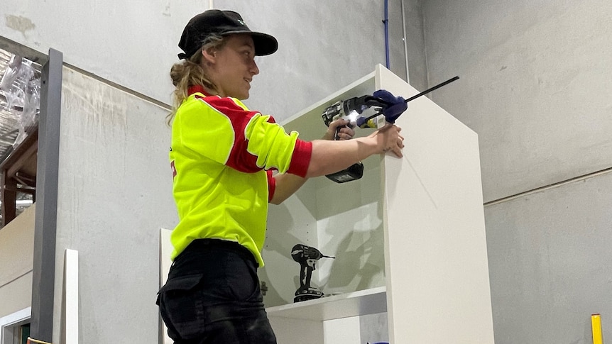 A female apprentice on a ladder working on a cabinet