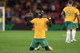 A male Socceroos player celebrates on his knees on the field.