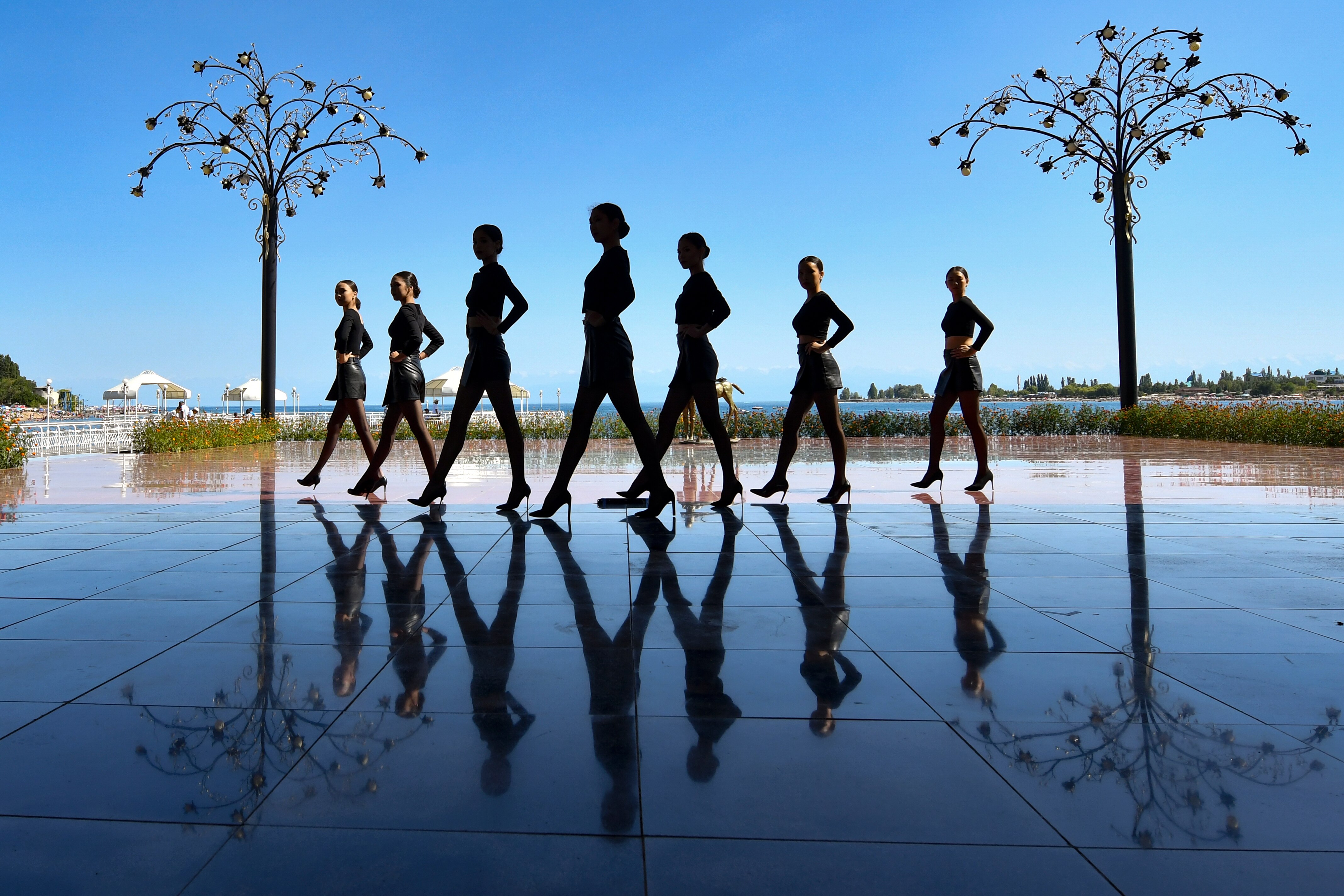 Silhouettes of seven female dancers in front of blue tiles and the sky. 