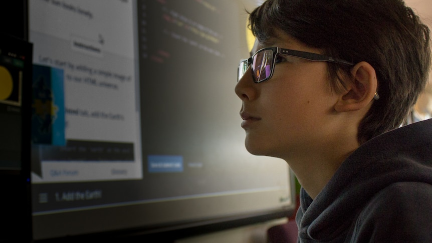 A boy using a computer, screen reflected in his spectacles.