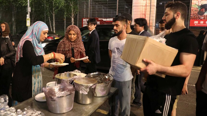 Food is distributed near a tower block severely damaged by a serious fire.