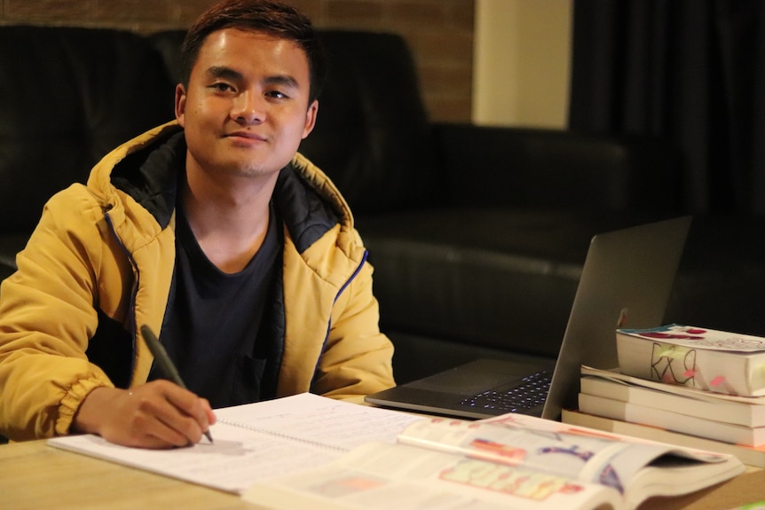 A student is seen sitting at a table with books and a laptop. 