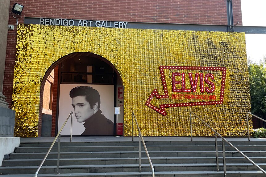 The wall is covered in gold glitter with a red Las Vegas-styled Elvis sign and a black and with picture of Elvis. 