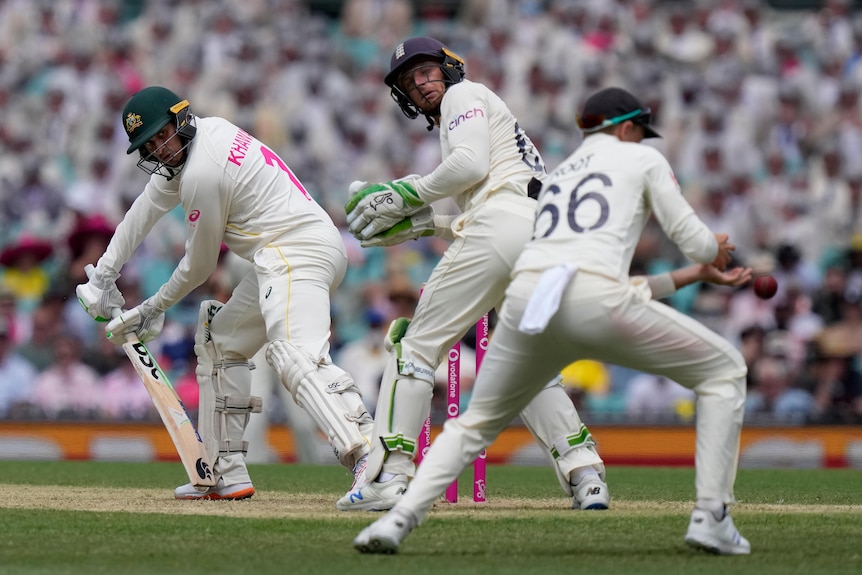 Australia batter Usman Khawaja (left) turns to see he is dropped by England fielder Joe Root (right) during a Test match.