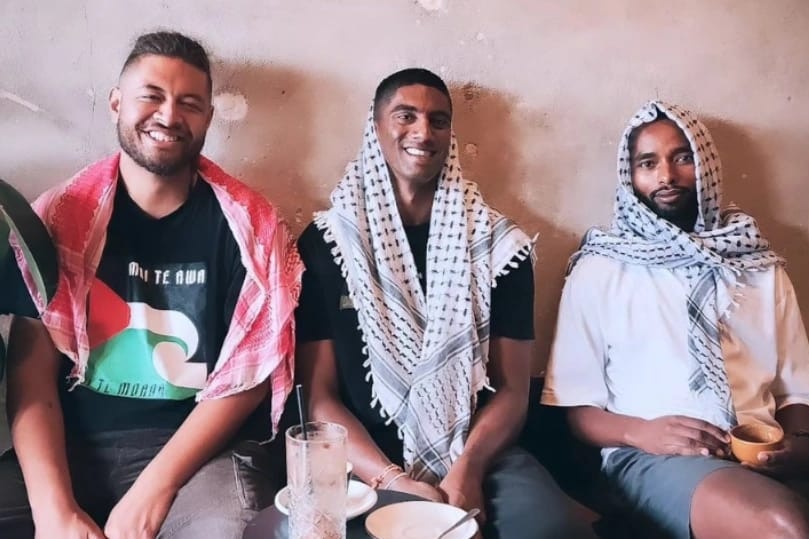 Three men sit, Suveen is in the middle. All three are wearing Palestinian scarfs.