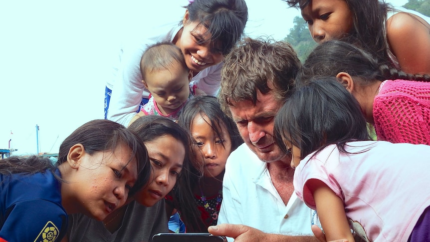A man with a satellite phone surrounded by women and children on an Indonesian island.