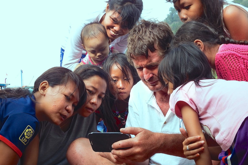 A man with a satellite phone surrounded by women and children on an Indonesian island.