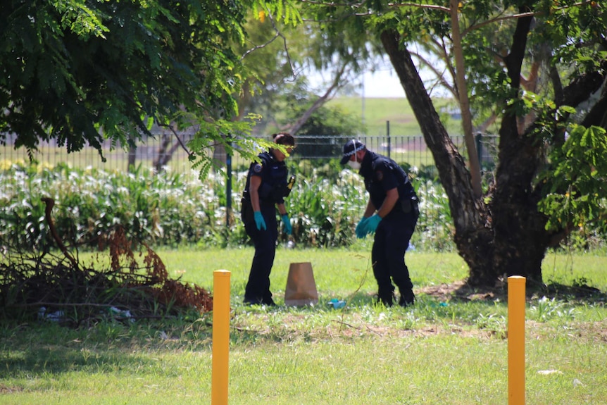 Two police officers crouch in a yard
